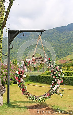 Beautiful basket swing of the wedding decorated with the colorful roses flower in the nature garden hanging on pole under tree Stock Photo