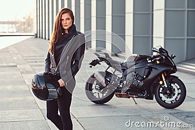 A beautiful biker girl holding helmet next superbike outside a building. Stock Photo