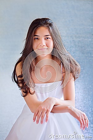 Beautiful biracial teen girl in white dress, sitting arms crossed Stock Photo
