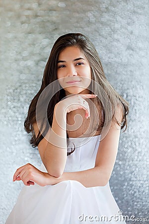 Beautiful biracial teen girl in white dress sitting, thinking Stock Photo