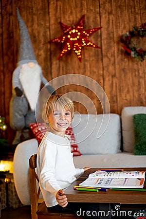 Beautiful blond child, young school boy, writing letter to Santa Claus in a decorated home with knitted toys Stock Photo