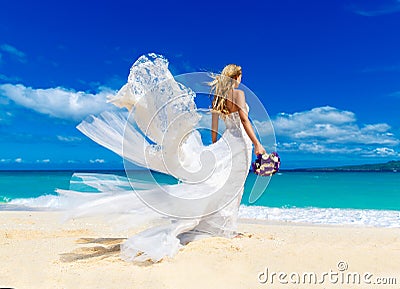 beautiful blond fiancee in white wedding dress with big long white train and with wedding bouquet stand on shore sea Stock Photo