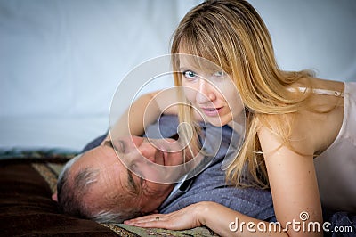 Beautiful Blond-Haired Woman in Lingerie Hugging Her Senior Husband Lying in Bed. Couple with Age Difference. Stock Photo