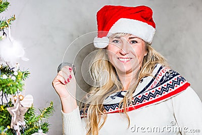 Beautiful blond middle age mom with blue eyes by the Chritmas tree with Santa hat and bell in the hand Stock Photo