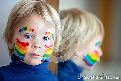 Beautiful blond toddler boy with rainbow painted on his face and messy hands Stock Photo