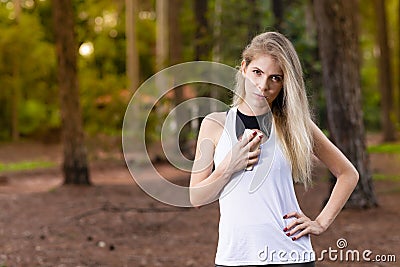 Beautiful blond young woman in park at sunset holding mobile near chest - Image Stock Photo