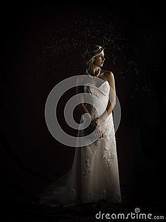 Beautiful blonde bride wearing vintage strapless wedding gown standing in the rain Stock Photo