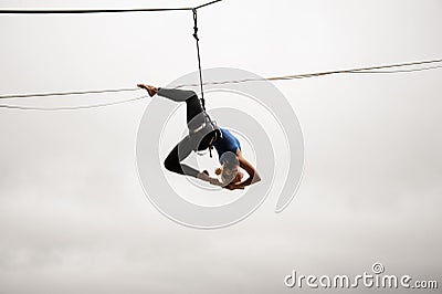 Beautiful blonde girl balancing high on a slackline against the grey sky and town Stock Photo