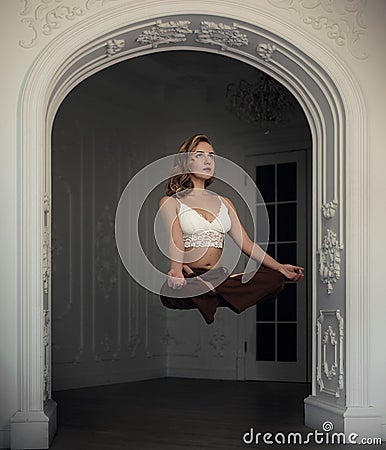 Beautiful blonde girl flies in the lotus position in white interior with arch. levitation magic. yoga pose. Stock Photo