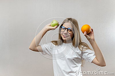 Beautiful blonde girl in a white T-shirt smiles and holds an apple and an orange in her hands. Healthy nutrition for Stock Photo