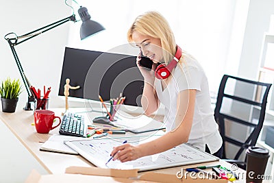 A young girl is standing near a table, talking on the phone and holding a marker in her hand. On the table is a magnetic Stock Photo