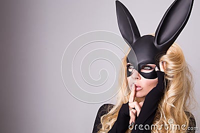 Beautiful blonde-haired young woman in carnival mask ballroom rabbit with long ears sensual in a black dress, standing defian Stock Photo
