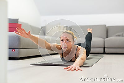 Beautiful blonde woman doing home workout indoors. Woman practice yoga at home. Fit girl using workout tutorials for Stock Photo