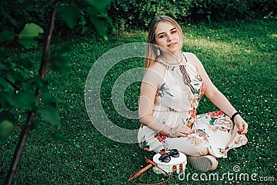 Beautiful blonde woman dressed in flower dress sitting on the green grass lawn. Copy, empty space for text Stock Photo