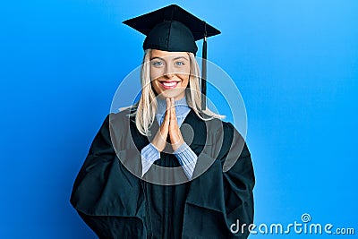 Beautiful blonde woman wearing graduation cap and ceremony robe praying with hands together asking for forgiveness smiling Stock Photo