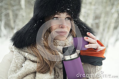 Beautiful blondy girl drink hot tea in a thermos in snowy forest Stock Photo