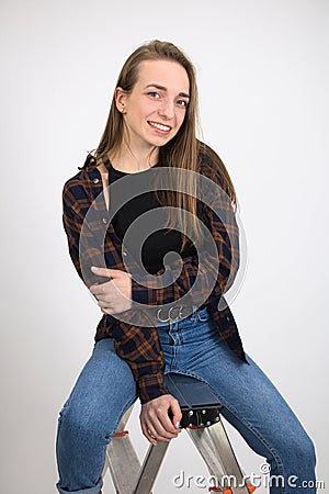 Beautiful smiling girl with long hair posing while sitting on a folding ladder. Stock Photo