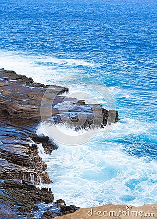 Beautiful blue ocean water hitting against rocky edge Stock Photo