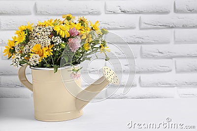 Beautiful bouquet of bright wildflowers in watering can on white wooden table near brick wall, space for text Stock Photo
