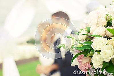 Beautiful bouquet of flowers on the background of a blurred silhouette of a loving couple of bride and groom. Stock Photo