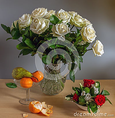 Beautiful bouquet of roses in a crystal jug and a pear with tangerines. Stock Photo