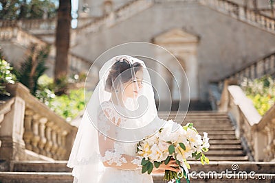 Beautiful bride covered with a veil with bridal bouquet on the stairs of the Nativity of the Blessed Virgin Mary church Stock Photo