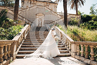 Beautiful bride covered with a veil with bridal bouquet on the stairs of the Nativity of the Blessed Virgin Mary church Stock Photo