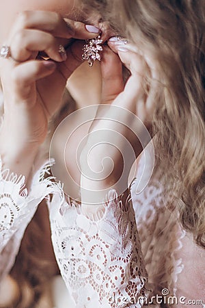 Beautiful bride in lace robe putting on luxury earrings, bridal Stock Photo