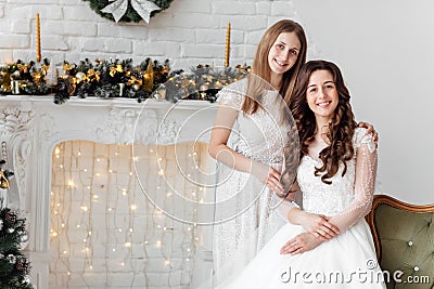 Beautiful bride in luxury wedding dress and pretty bridesmaid in dresse in decorated christmas studio. weddind in Christmas Stock Photo