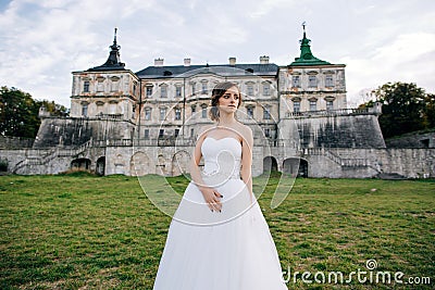 Beautiful bride in white dress stands against the backdrop of an old palace in Europe Stock Photo