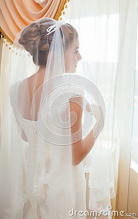 Bride in white wedding dress standing near the window Stock Photo
