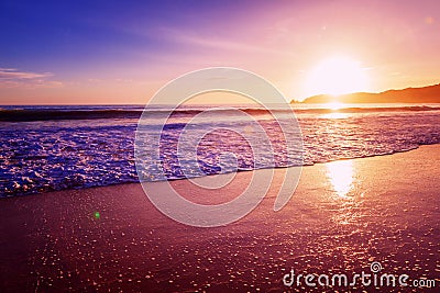 Beautiful bright purple purple sunset on the ocean, sandy beach, waves and glare of the sun Stock Photo
