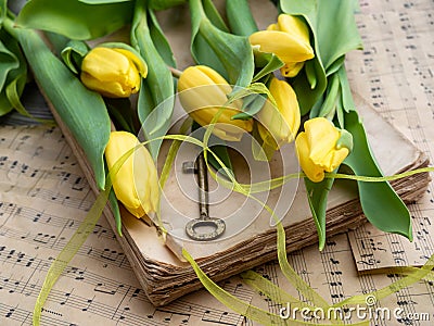 Beautiful bright yellow tulips laying on old book and musical note sheet. Stock Photo