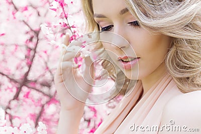 Beautiful bright young happy cute girl walks in the park near the pink flowering tree in a sunny day Stock Photo