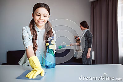 Beautiful brunette caucasian mother and daughter cleaning together in room. Girl hold spray in hands and clean table Stock Photo