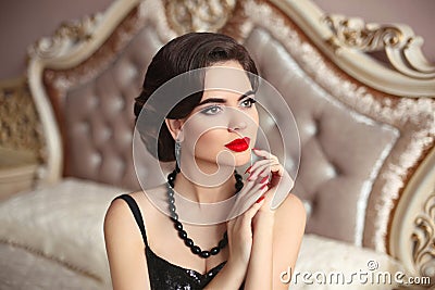 Beautiful brunette, elegant woman portrait. Manicure nails. Retro lady with red lips makeup, wavy hairstyle posing on modern bed Stock Photo