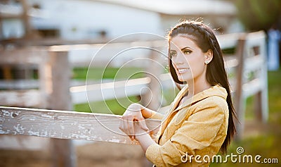 Beautiful brunette girl with long hair smiling near an old wooden fence. Stock Photo