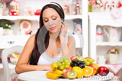 Beautiful brunette girl sitting at the kitchen table with a plate of fresh fruit. Stock Photo