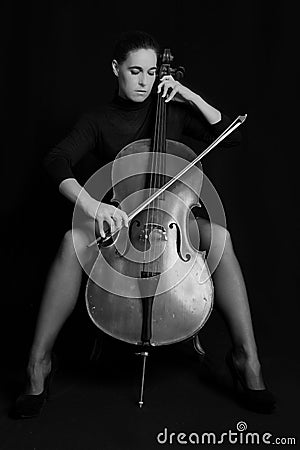 Beautiful brunette playing a cello with selective light in black Stock Photo