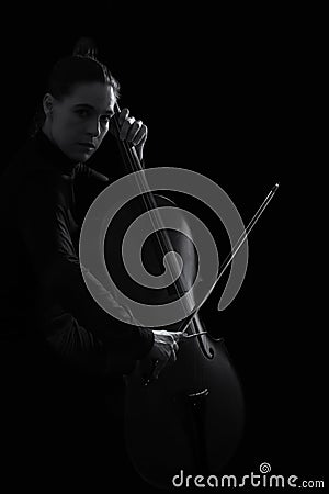 Beautiful brunette playing a cello with selective light in black Stock Photo