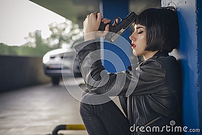 Beautiful brunette sexy spy agent killer or police woman in leather jacket and jeans with a gun in her hand running after Stock Photo