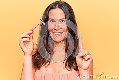 Beautiful brunette woman asking for depilation holding shaver razor over yellow background smiling with an idea or question Stock Photo