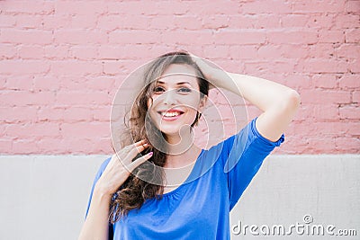 A beautiful brunette woman in a blue blouse posing against a textured pink brick wall. Portrait of a young woman Stock Photo