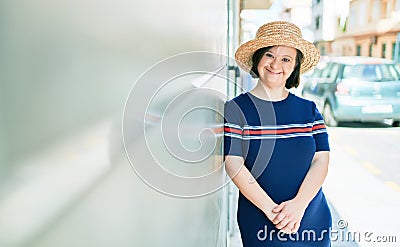 Beautiful brunette woman with down syndrome at the town on a sunny day wearing summer hat leaning on the wall Stock Photo
