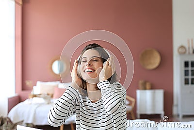 Beautiful brunette woman in earphones sitting on sofa listening to music with closed eyes Stock Photo