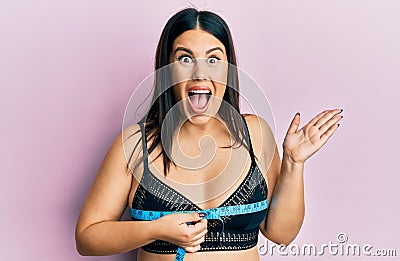 Beautiful brunette woman using tape measure measuring breast celebrating achievement with happy smile and winner expression with Stock Photo