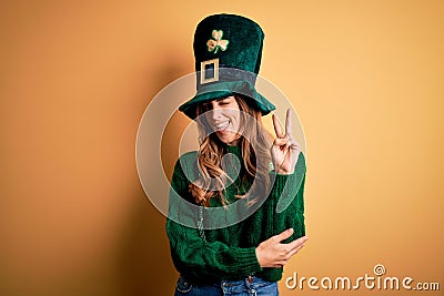 Beautiful brunette woman wearing green hat with clover celebrating saint patricks day smiling with happy face winking at the Stock Photo