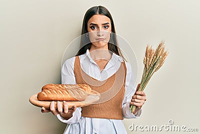 Beautiful brunette young woman holding homemade bread and spike wheat depressed and worry for distress, crying angry and afraid Stock Photo