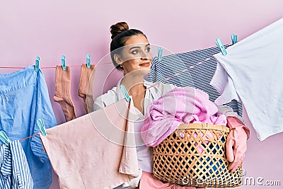 Beautiful brunette young woman holding laundry basket smiling looking to the side and staring away thinking Stock Photo