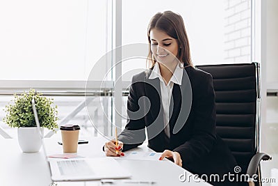 Beautiful business lady is looking at laptop and smiling while working in office. Concentrated on work Stock Photo